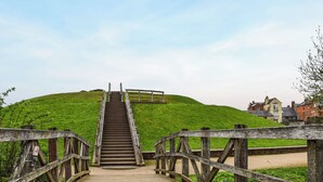 Eine Holztreppe führt einen grasbewachsenen Hügel hinauf, beidseits verläuft ein Holengeländer.