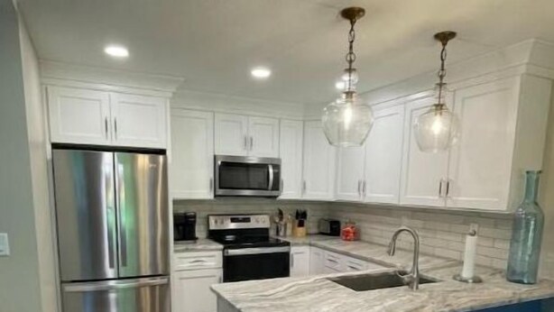 A modern kitchen with white cabinets, stainless steel appliances, a marble island, and bar stools.