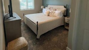 A bedroom with a bed, a desk, a chair, a ceiling fan, and a window.