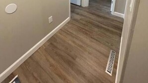 A hallway with wooden flooring, a light-colored wall, and a decorative piece.