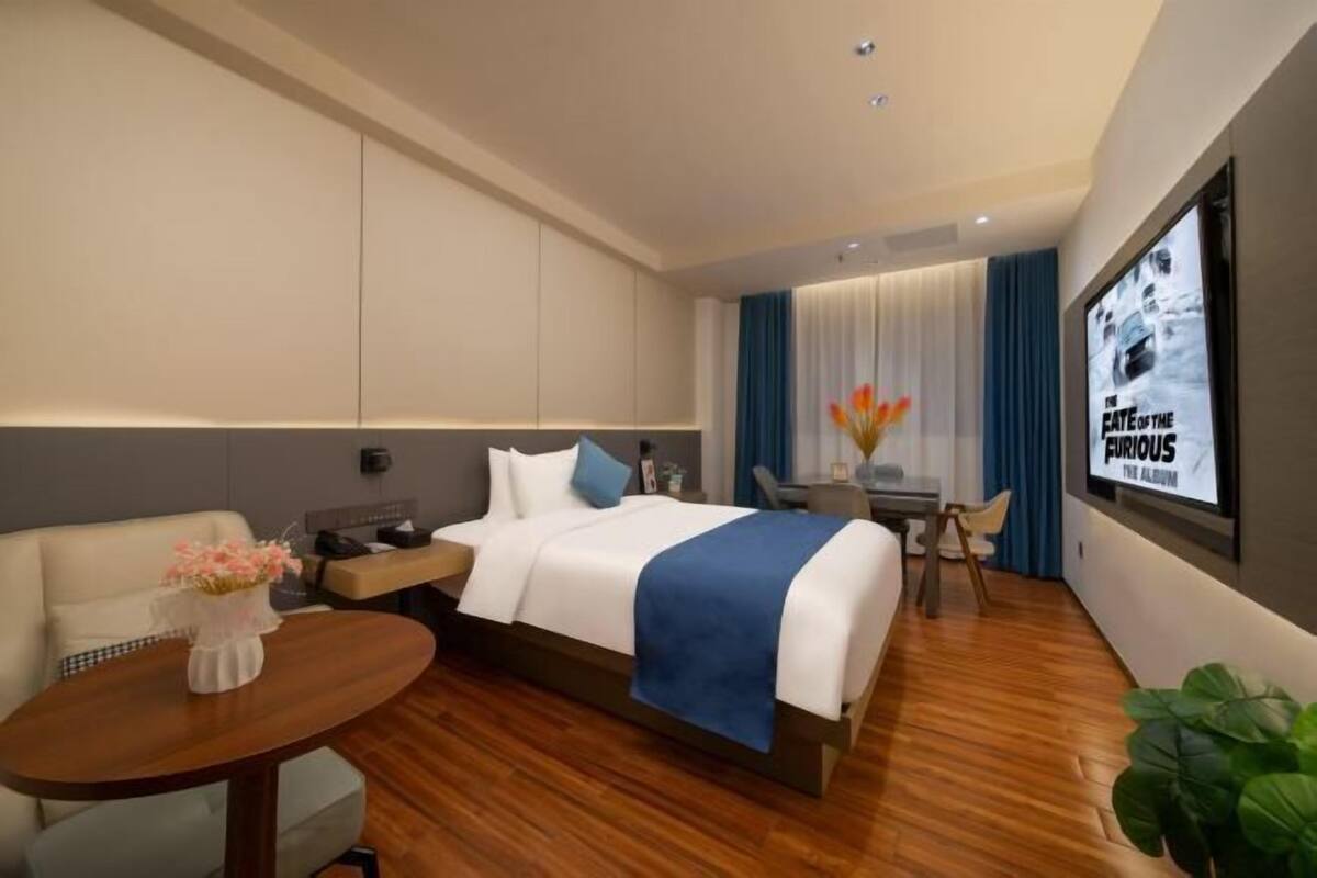 A modern hotel room with a large bed, a desk, a chair, and a TV screen displaying a movie poster.
