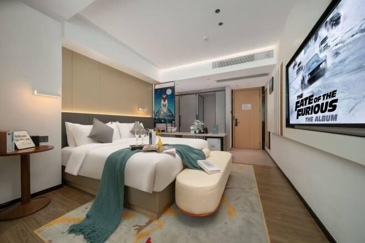 A modern hotel room with a bed, a desk, and a large poster of 'The Fate of the Furious' album.