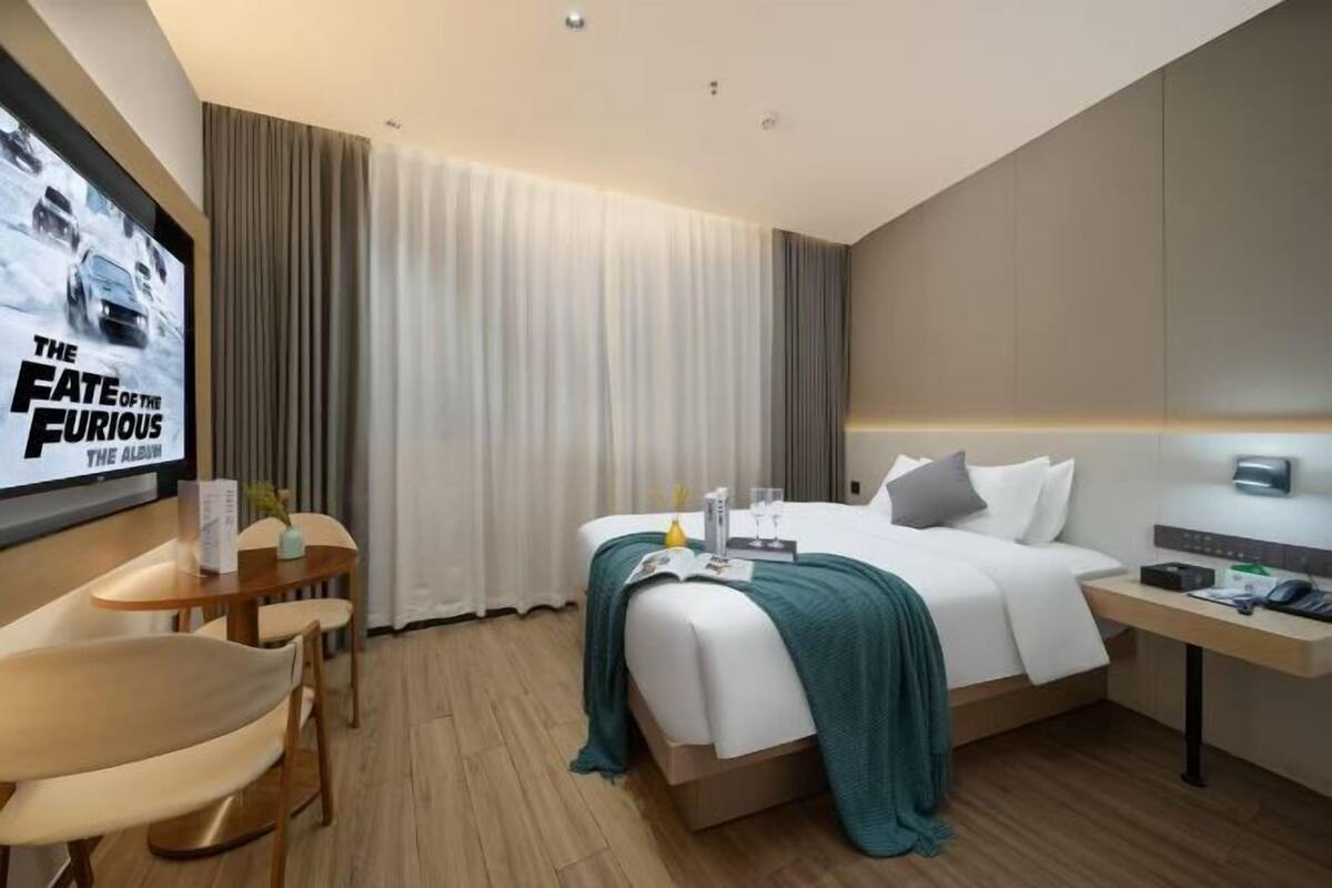 A hotel room with a bed, a desk, a chair, a TV, and a window with curtains.