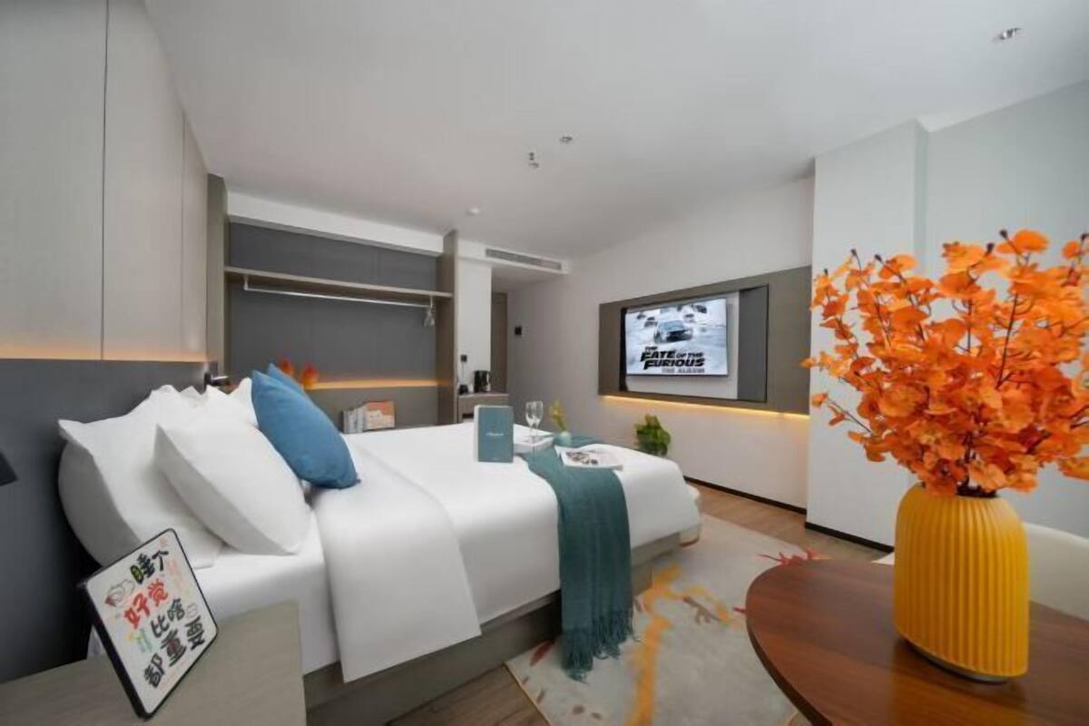 A modern hotel room with a bed, a desk, a TV, and a decorative vase.