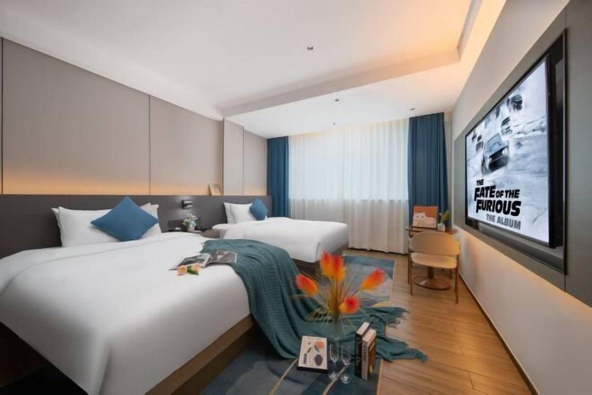 A hotel room with two beds, a flat-screen TV, a vase with flowers, and a poster on the wall.