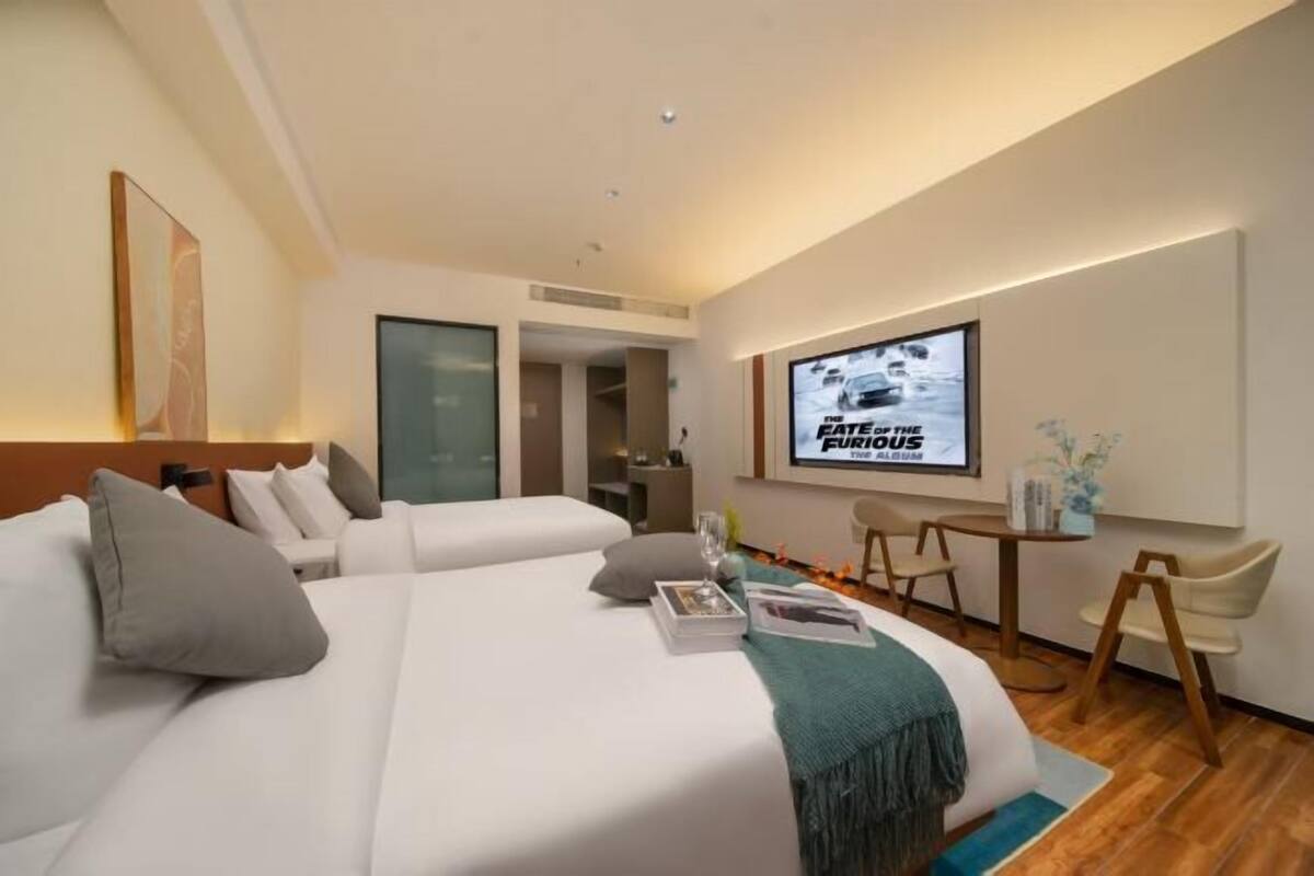 A hotel room with two beds, a TV screen, a desk, and a chair.