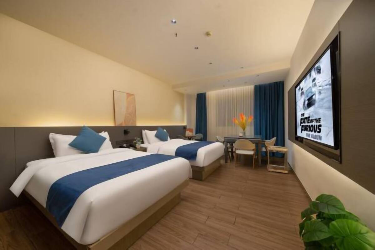 A hotel room with two beds, a desk, and a TV screen displaying 'The Fate of the Furious'.