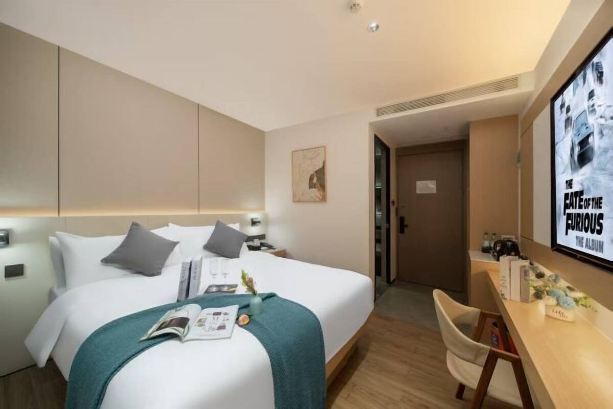 A modern hotel room with a large bed, a desk, and a TV displaying 'The Fast and the Furious' movie.