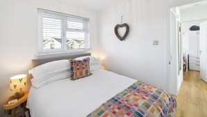 A bedroom with a bed, a window with blinds, a wall-mounted heart decoration, a hanging light fixture, and a door leading to another room. - 2 bedroom accommodation in Newquay (Newquay)