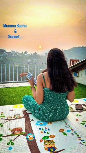 Una mujer sentada en un balcón contemplando la puesta de sol, vestida con un vestido verde.