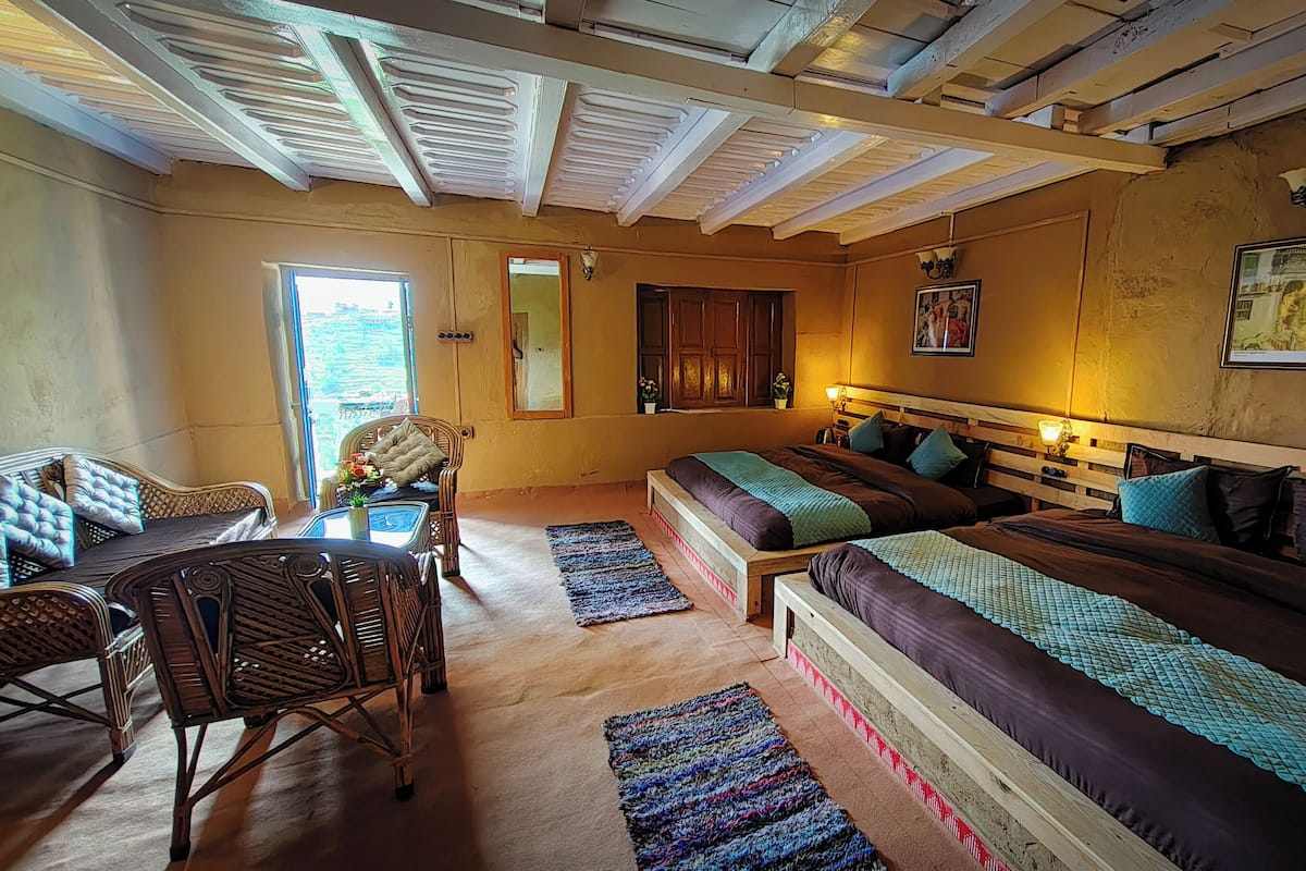 A cozy bedroom with a large bed, a wooden headboard, a small table with chairs, and a window with curtains.