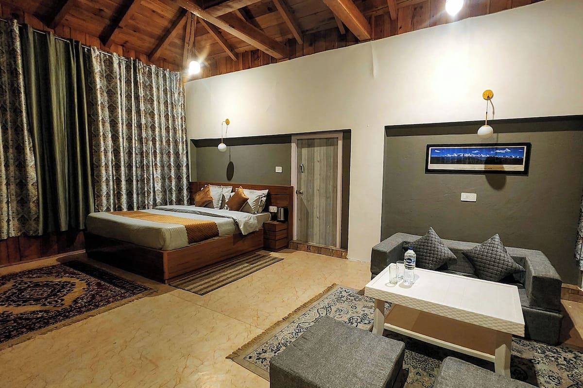 A bedroom with a bed, a sofa, a small table, and a TV on the wall.