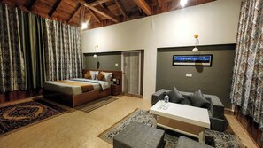 Un dormitorio con cama, sofá, una mesita y televisor en la pared.