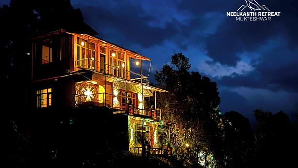 A multi-story building with illuminated windows and a balcony, surrounded by trees.