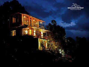 A multi-story building with illuminated windows and a balcony, surrounded by trees. - Neelkanth retreat (Dhari)