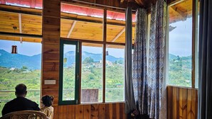 A rustic wooden room with large windows, a bed, and a chair.