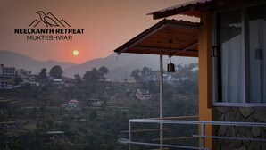 A view from a balcony at Neelkanth Retreat in Mukteshwar, featuring a sunset over a hilly landscape with terraced fields and buildings. - Neelkanth retreat (Dhari)