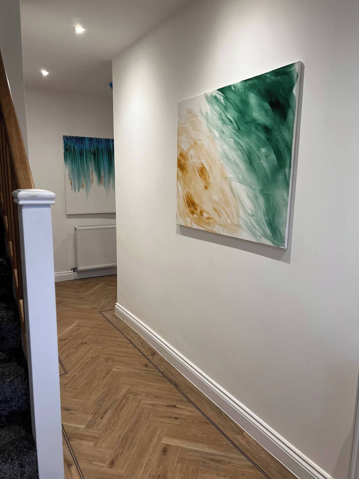 A hallway with a wooden floor, white walls, and a large abstract painting.