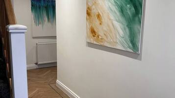 A hallway with a wooden floor, white walls, and a large abstract painting.
