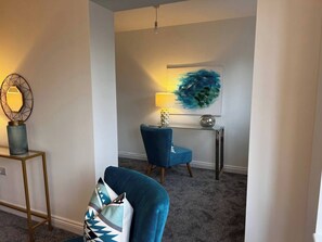 A modern living room with a blue armchair, a glass coffee table, and a painting on the wall. - Long Shoot - Beautiful, spacious and luxurious house. (Nuneaton)