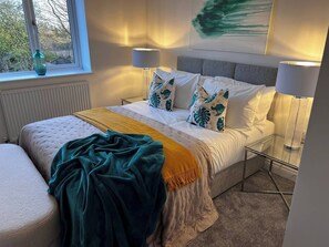 A modern bedroom with a bed, two bedside lamps, a window with a view, and a decorative plant. - Long Shoot - Beautiful, spacious and luxurious house. (Nuneaton)