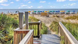Une promenade en bois mène à une plage agrémentée de parasols colorés et d’une zone de plage de sable.