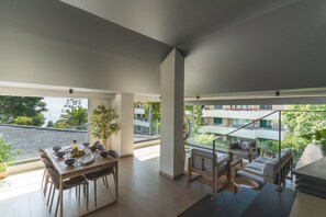 Zona pranzo moderna con tavolo in legno apparecchiato per quattro persone, circondato da sedie. Si nota una scala che conduce a un livello superiore con un balcone.