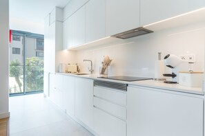 A modern kitchen with white cabinetry, a built-in oven, and a large window overlooking a cityscape. - Babi by the Sea by Atlantic Holiday (Funchal)