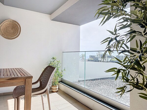 Un balcón con una mesa y sillas de madera, un tapiz tejido y una planta en maceta.