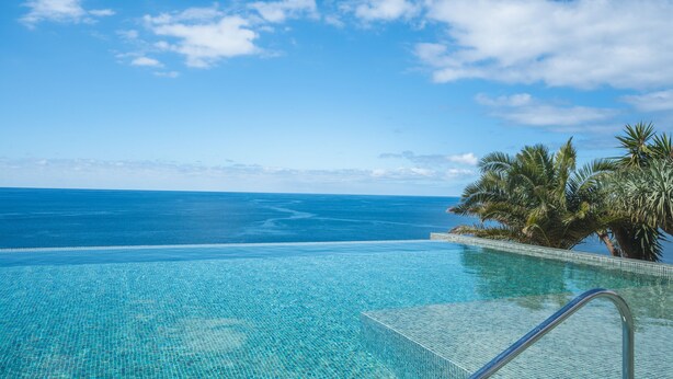Una piscina cristallina con vista sull'oceano e palme.