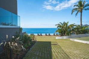 A patio with a view of the ocean, lounge chairs, palm trees, and a modern building with glass windows. - Babi by the Sea by Atlantic Holiday (Funchal)