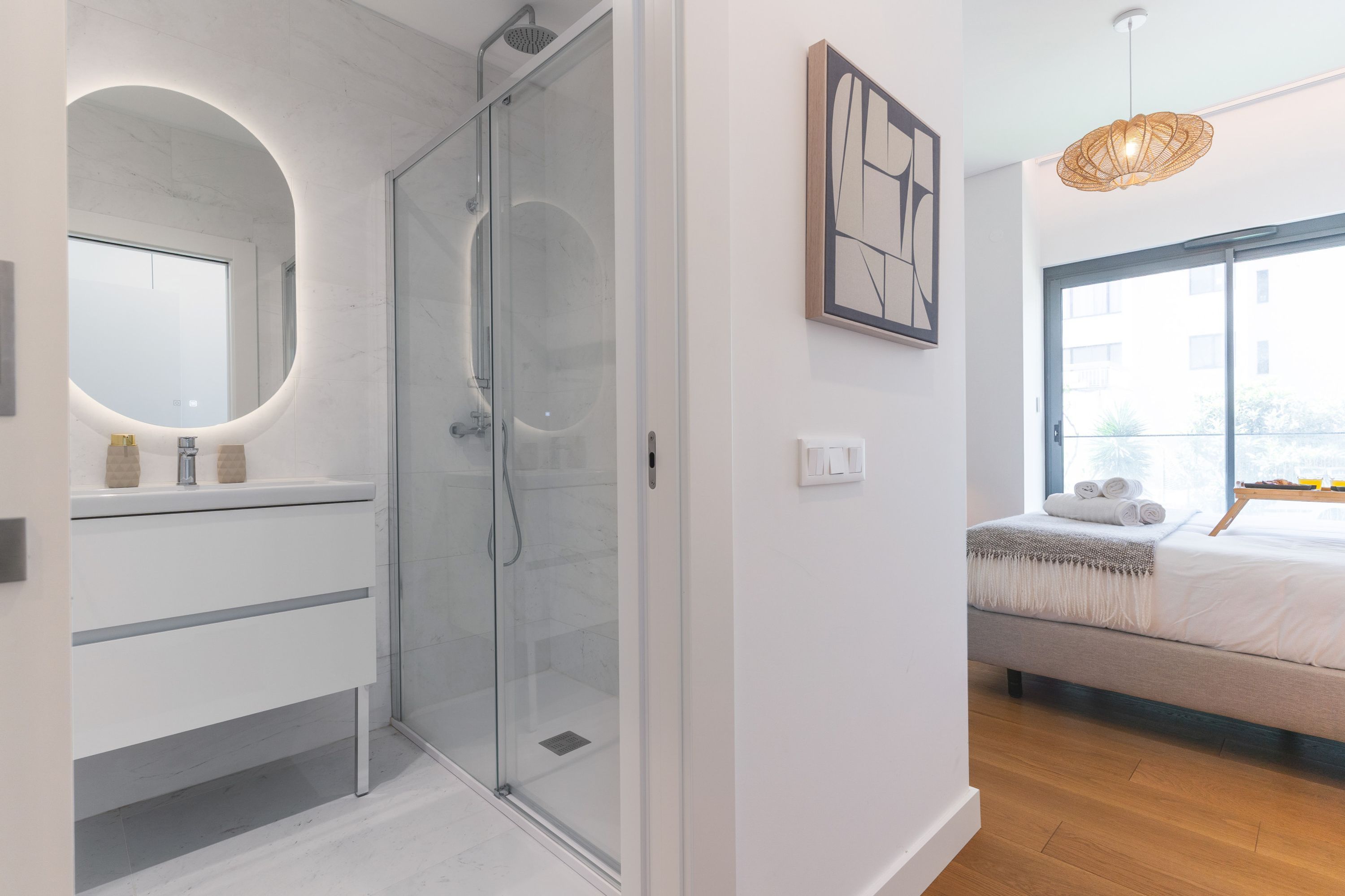 Une salle de bain moderne avec une douche à parois de verre, un miroir rond et une table de chevet avec un lit.
