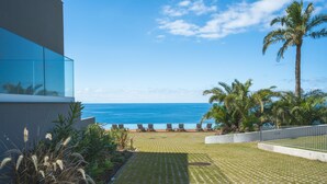 Una veranda con vista sull'oceano, sedie a sdraio, palme e un edificio moderno con finestre in vetro.
