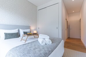 A modern bedroom with a large bed, a bedside table with a tray of toiletries, and a neatly made bed with rolled towels. - Babi by the Sea by Atlantic Holiday (Funchal)