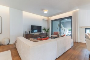 A modern living room with a sofa, a TV, and a glass door leading to a balcony. - Babi by the Sea by Atlantic Holiday (Funchal)