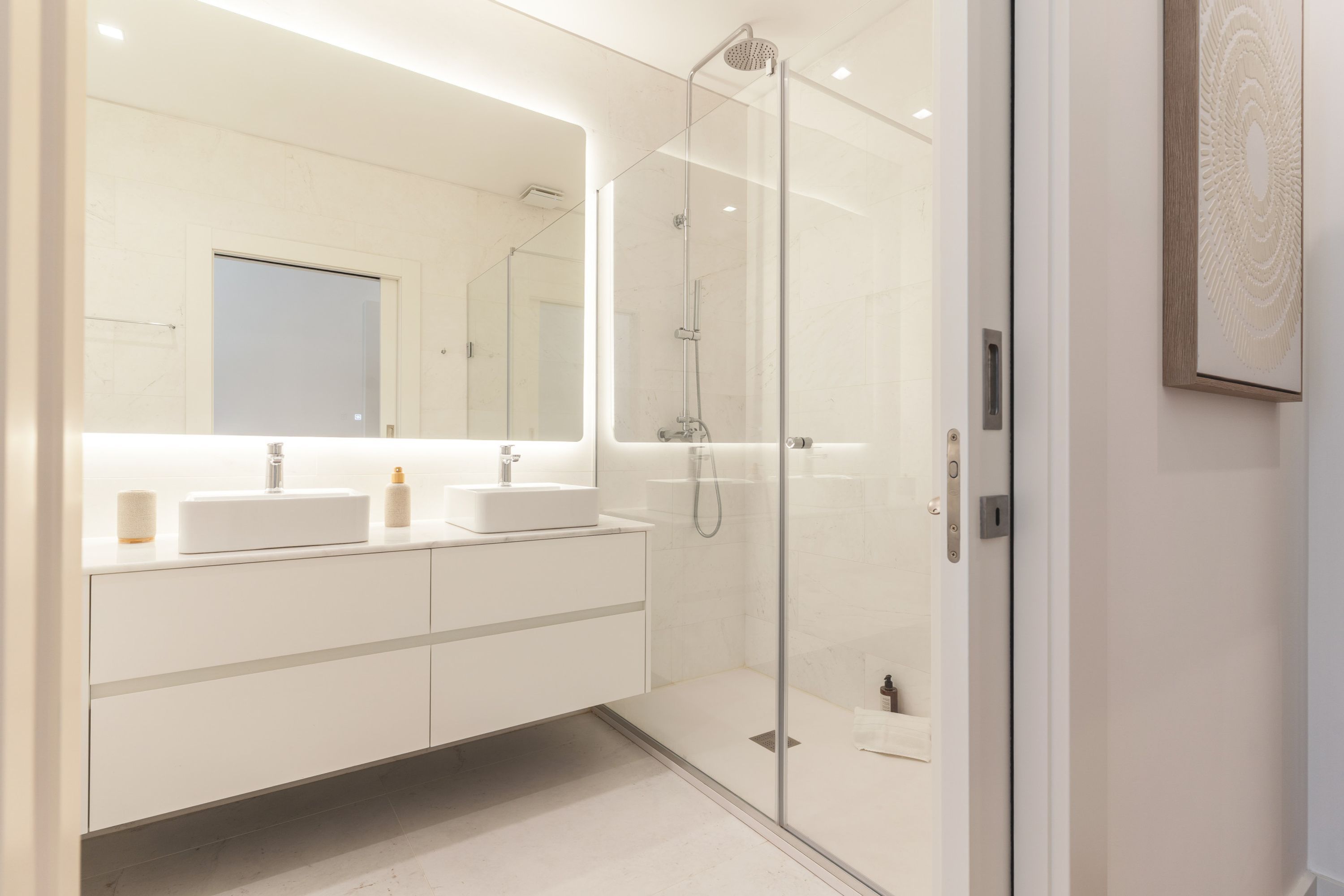 A modern bathroom with a glass-enclosed shower, a large mirror, and a white vanity with two sinks.