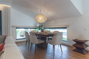 A dining area with a round table, six chairs, a hanging light fixture, and a view through large windows. - Babi by the Sea by Atlantic Holiday (Funchal)