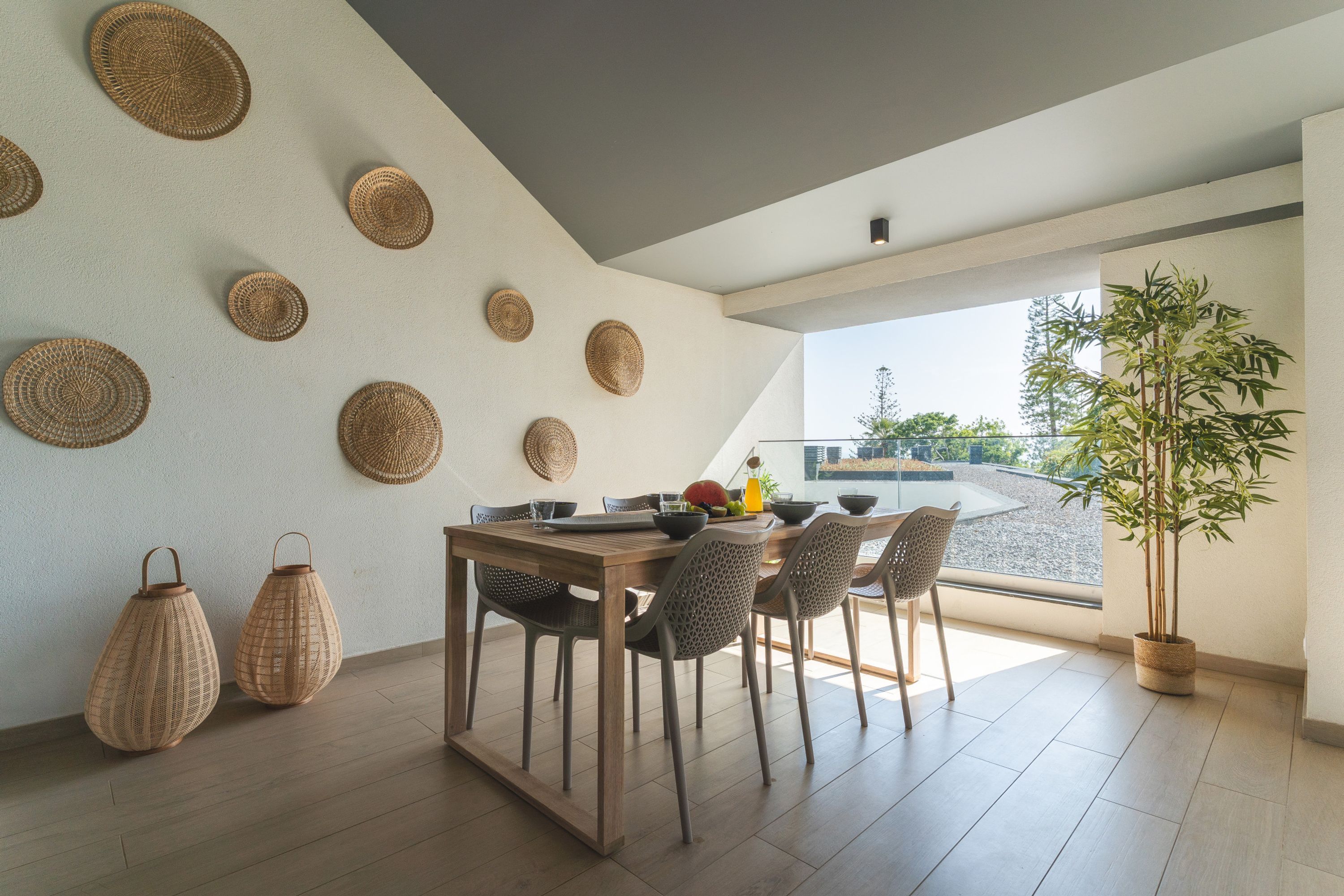 Un comedor con mesa de madera, adornos de pared tejidos y una planta en maceta.