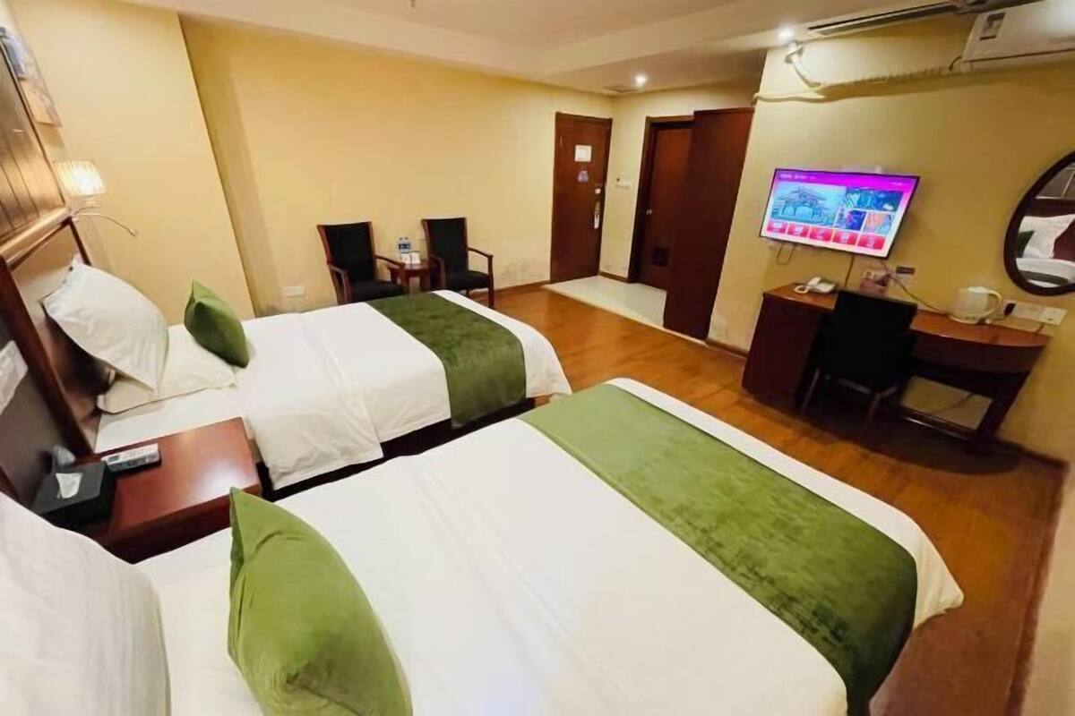 A hotel room with two beds, a desk with a computer, a TV, and a mirror.
