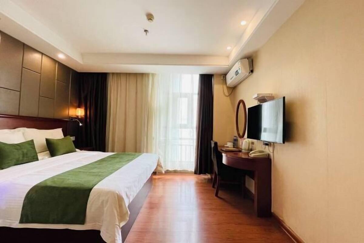 A hotel room with a bed, a desk, a chair, a television, and an air conditioning unit.