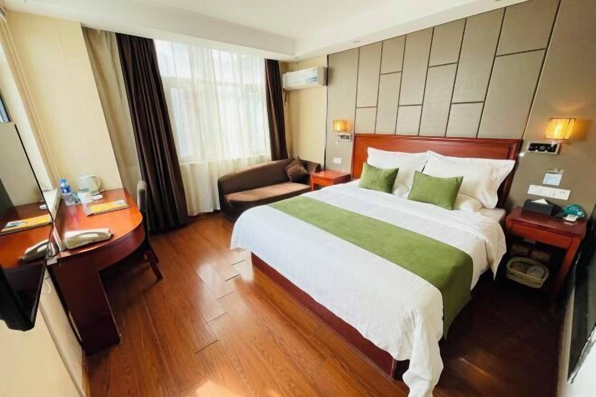 A hotel room with a bed, a desk, a chair, a TV, and a window with curtains.