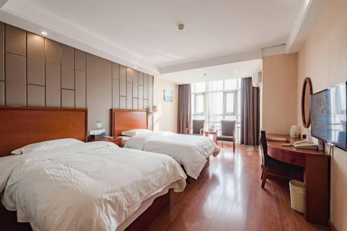 A hotel room with two beds, a desk, a chair, and a TV.