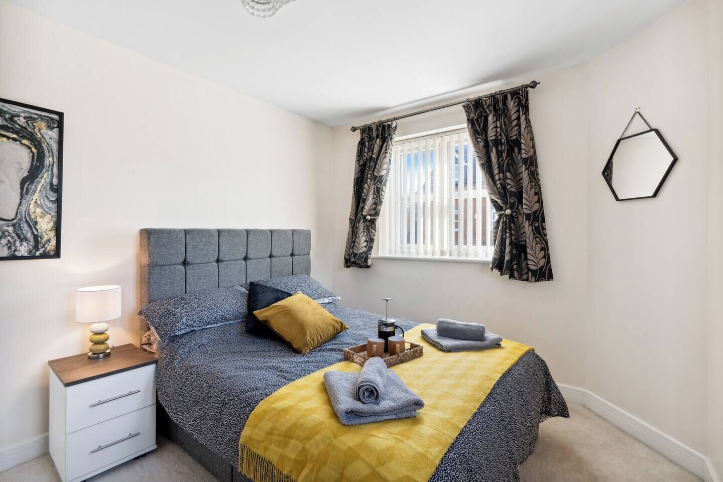 A bedroom with a bed, bedside table, lamp, and a window with curtains.