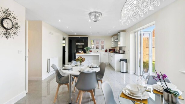 A modern kitchen with white cabinets, a built-in oven, and a dining area with a round table and chairs. - Olympic House - Spacious house for a weekend with friends (Hinckley)