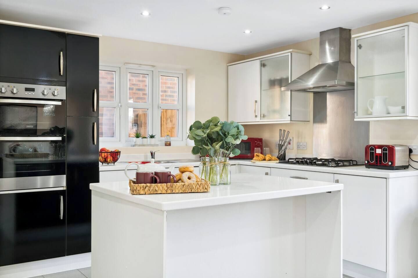 A modern kitchen with a central island, black and white cabinetry, stainless steel appliances, and a view of the outdoors through large windows.