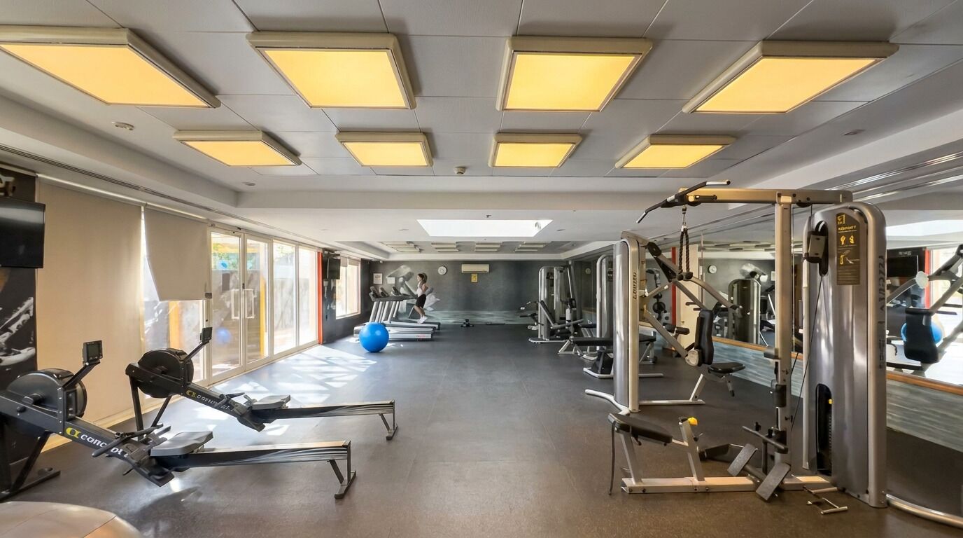 Ein Fitnessstudio mit unterschiedlichen Trainingsgeräten, großen Fenstern und einer Spiegelwand.