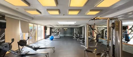 A gym with various exercise equipment, large windows, and a mirrored wall.