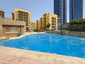 A swimming pool with a basketball court, surrounded by high-rise buildings.