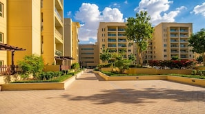 A multi-story residential building with a central courtyard, surrounded by greenery and a clear sky. - Vogue, Al Alka Greens near Mall of the Emirates (Dubai)