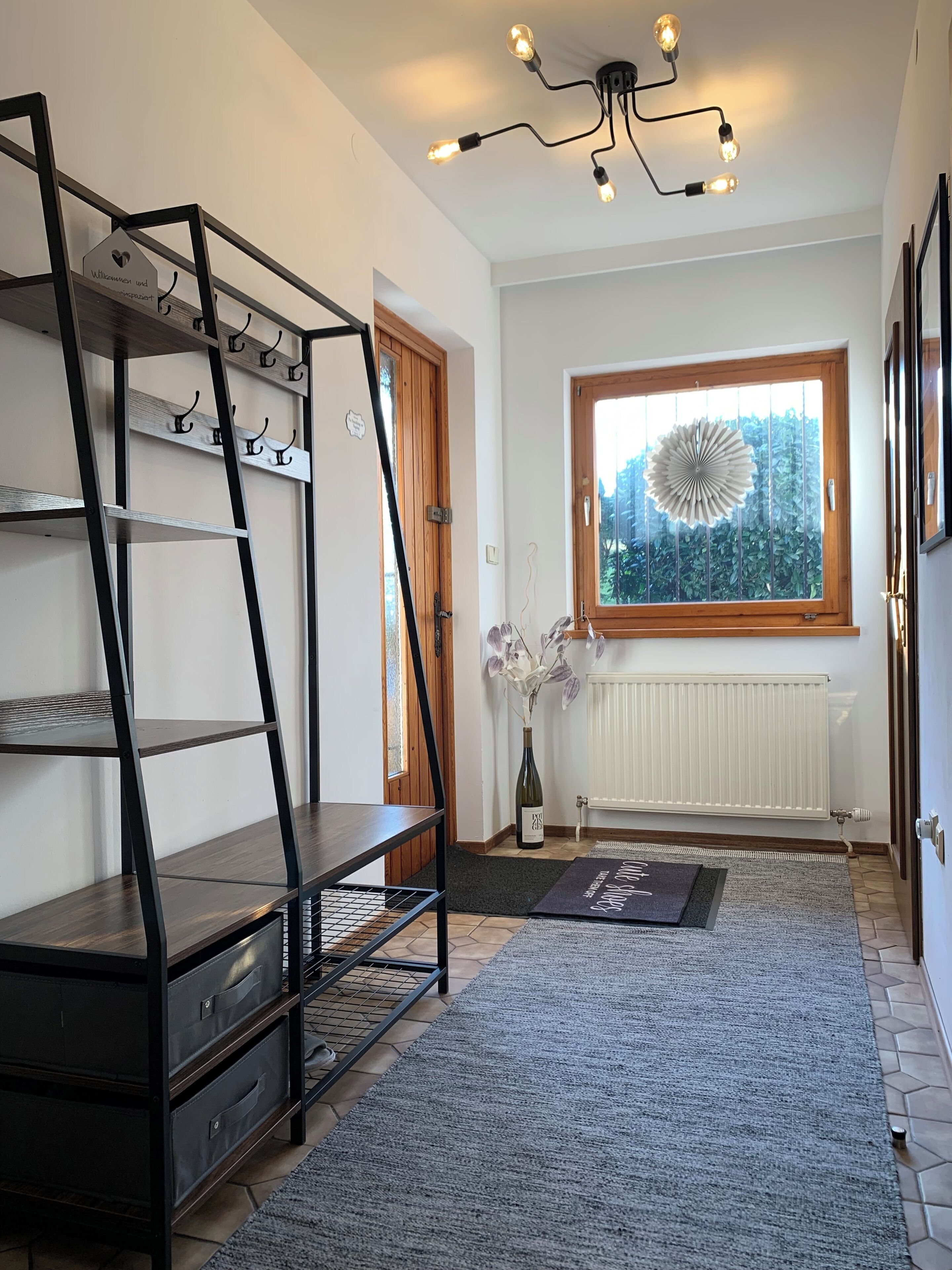 A modern room with a black metal shelving unit, a wooden door, a window with a view of greenery, and a radiator.